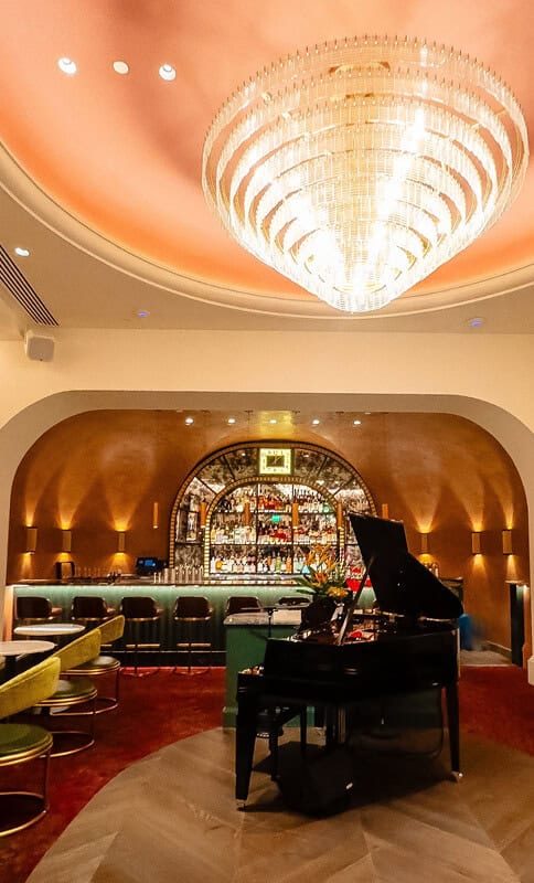 Elegant hotel lounge with a grand chandelier, bar area, and a black grand piano, perfect for sophisticated gatherings and live entertainment.