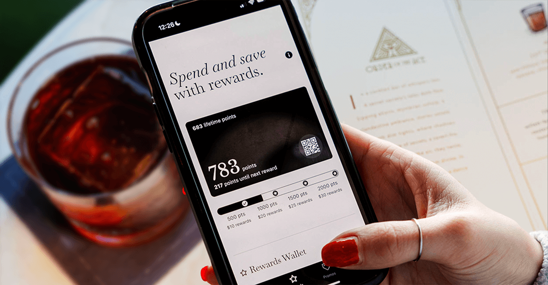 Loyalty rewards app on smartphone screen showing points balance, benefits for spending and saving with rewards, with a glass of soda and menu in the background.